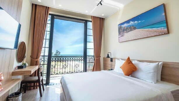 Quarto de hotel com cama grande, escrivaninha, cadeira, TV e varanda vista para a praia.