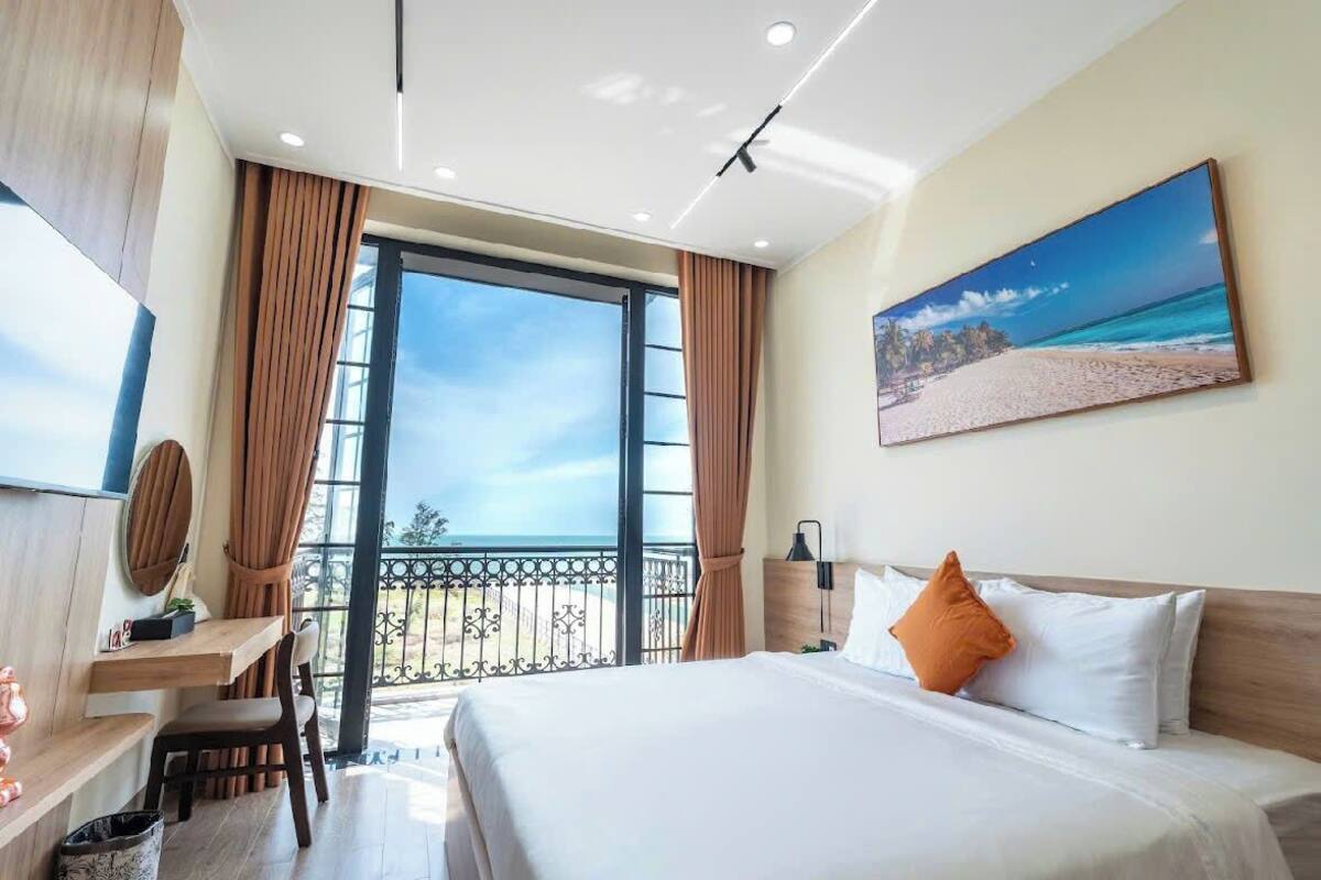 Une chambre d’hôtel avec un grand lit, un bureau, une chaise, une télévision et un balcon donnant sur la plage.