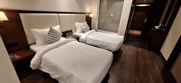A hotel room with two beds, a nightstand, a window with a view, and a door leading to a bathroom.