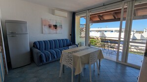 Un balcon avec une table et des chaises, un canapé, un réfrigérateur et une vue sur les bâtiments et la verdure.
