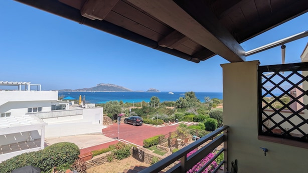 Un balcon donnant sur la mer, une voiture garée dans l’allée et un immeuble à la façade blanche.