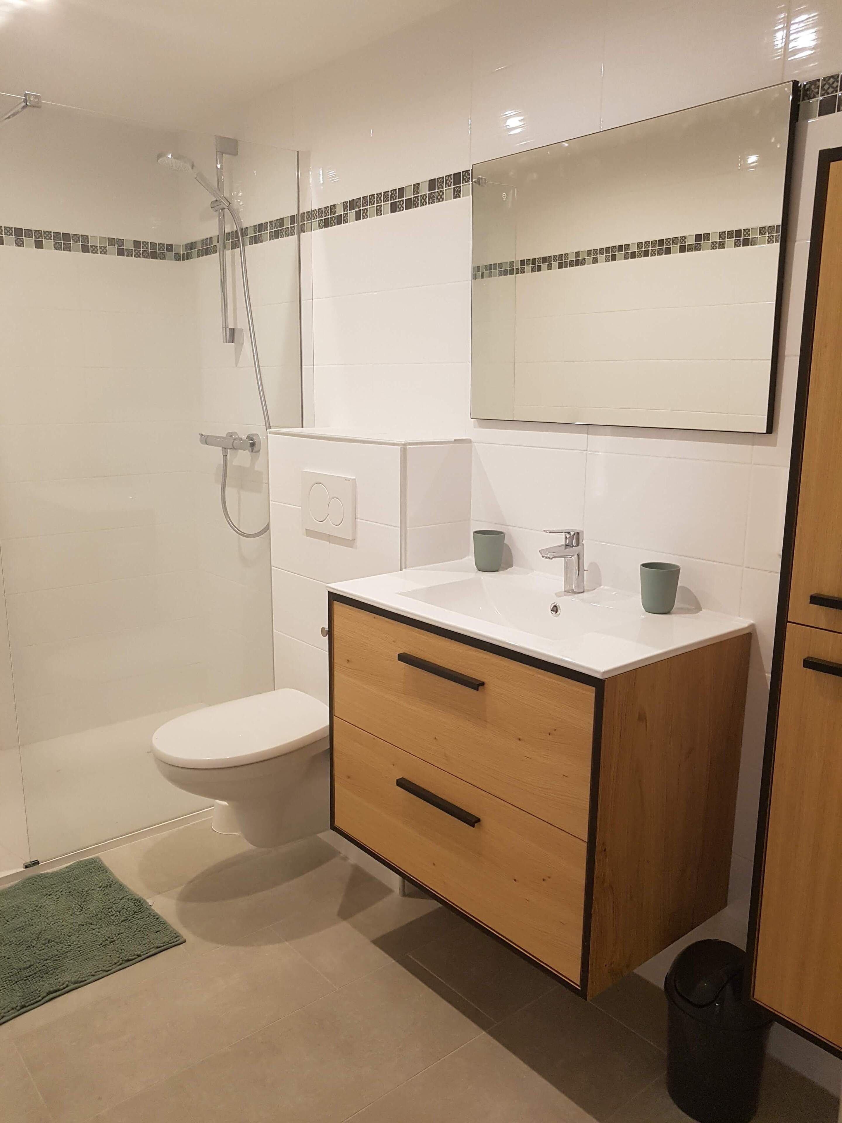 Et badeværelse med bruser, toilet, vaskebord med spejl og en skraldespand.