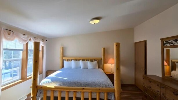 Ein Schlafzimmer mit einem hölzernen Bettgestell, einer Nachttischlampe, einem Spiegel und einem Fenster mit Vorhängen.