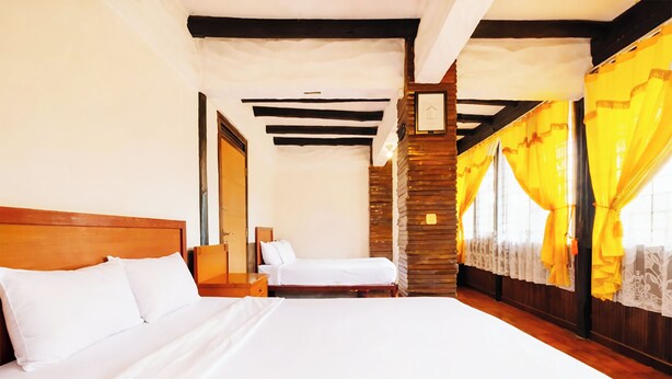 A hotel room with a large bed, a wooden headboard, a nightstand, a mirror, and a window with yellow curtains. - Cottage Syariah GS Rumah Kayu (Parongpong)