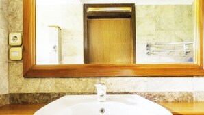 A bathroom with a white sink, a wooden-framed mirror, and a marble-tiled wall. - Cottage Syariah GS Rumah Kayu (Parongpong)