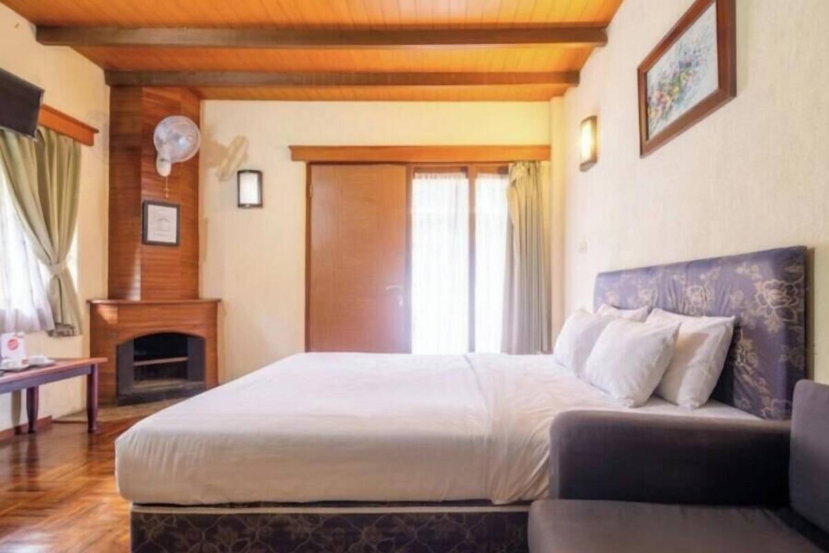 A bedroom with a bed, a sofa, a fireplace, and a large window.