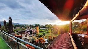A balcony with a view of a garden and distant buildings, a staircase, and a railing. - Cottage Syariah GS Rumah Kayu (Parongpong)