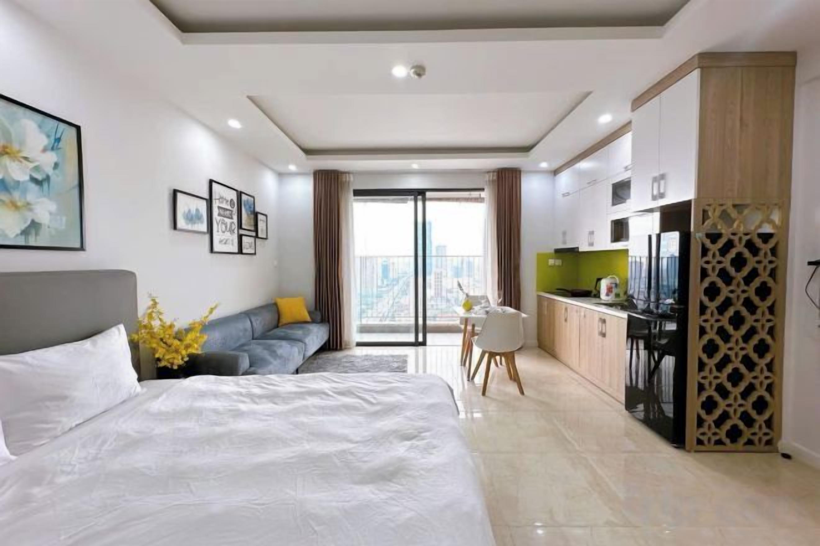 A modern hotel room with a large bed, a seating area, a kitchenette, and a view of the city.