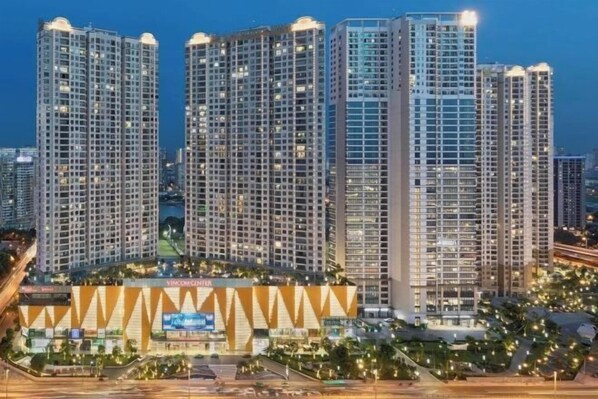 A high-rise building complex with multiple residential towers, a central building with a distinctive geometric facade, and a well-lit surrounding area. - Mei Housing - Vinhomes D'Capitale Residence Hanoi Central (Hanoi)