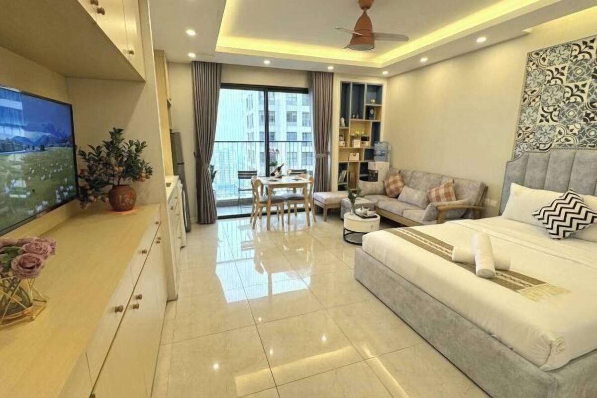 A modern bedroom with a large bed, a sofa, a dining table, and a TV.