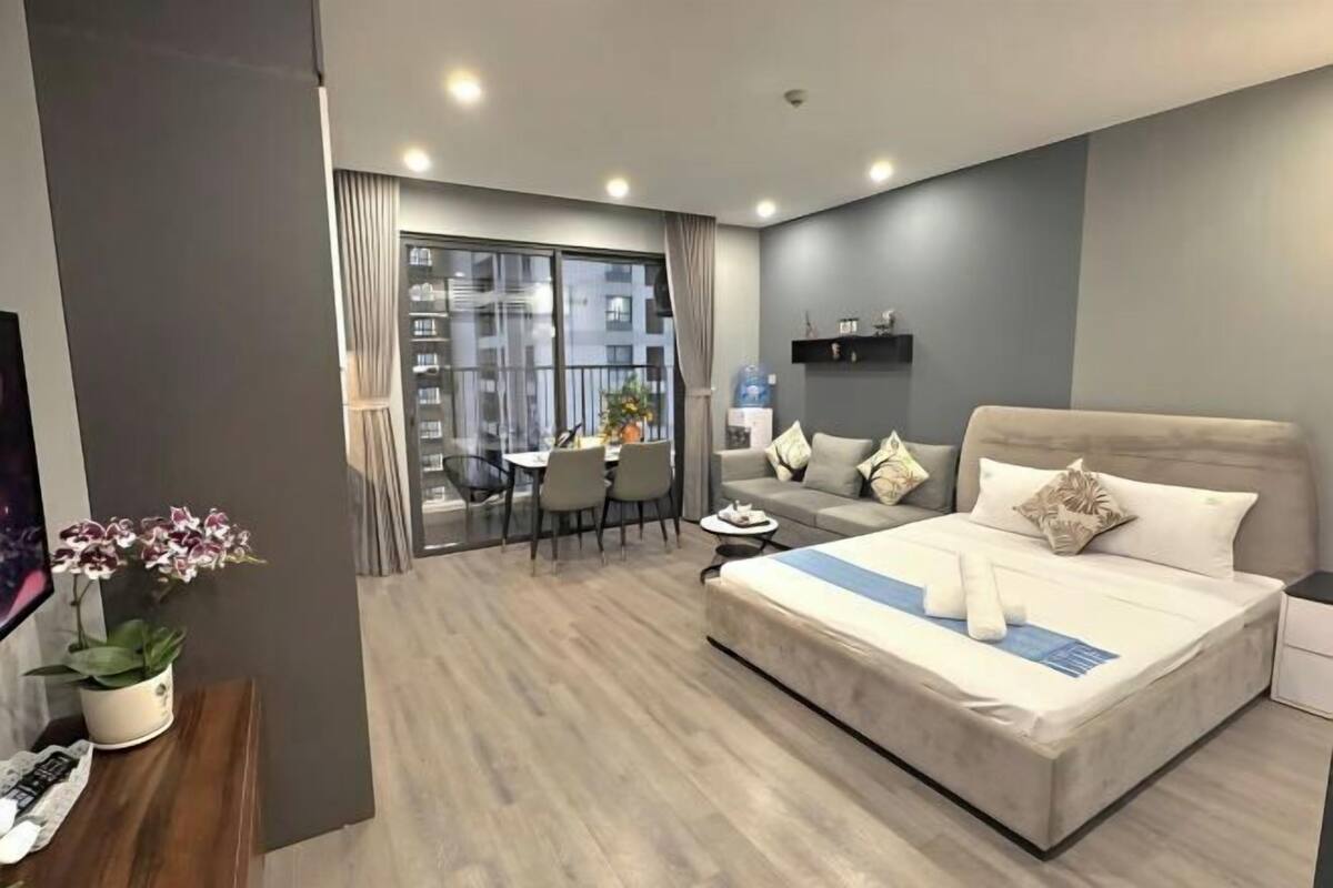A modern hotel room with a large bed, a sofa, a dining table, and a balcony with a view.