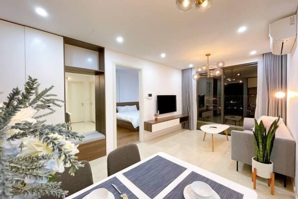 A modern hotel room with a dining area, a TV, a sofa, and a large window.