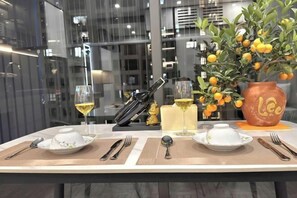 A dining table set with plates, cutlery, a vase with lemons, and a bottle of champagne. - Mei Housing - Vinhomes D'Capitale Residence Hanoi Central (Hanoi)