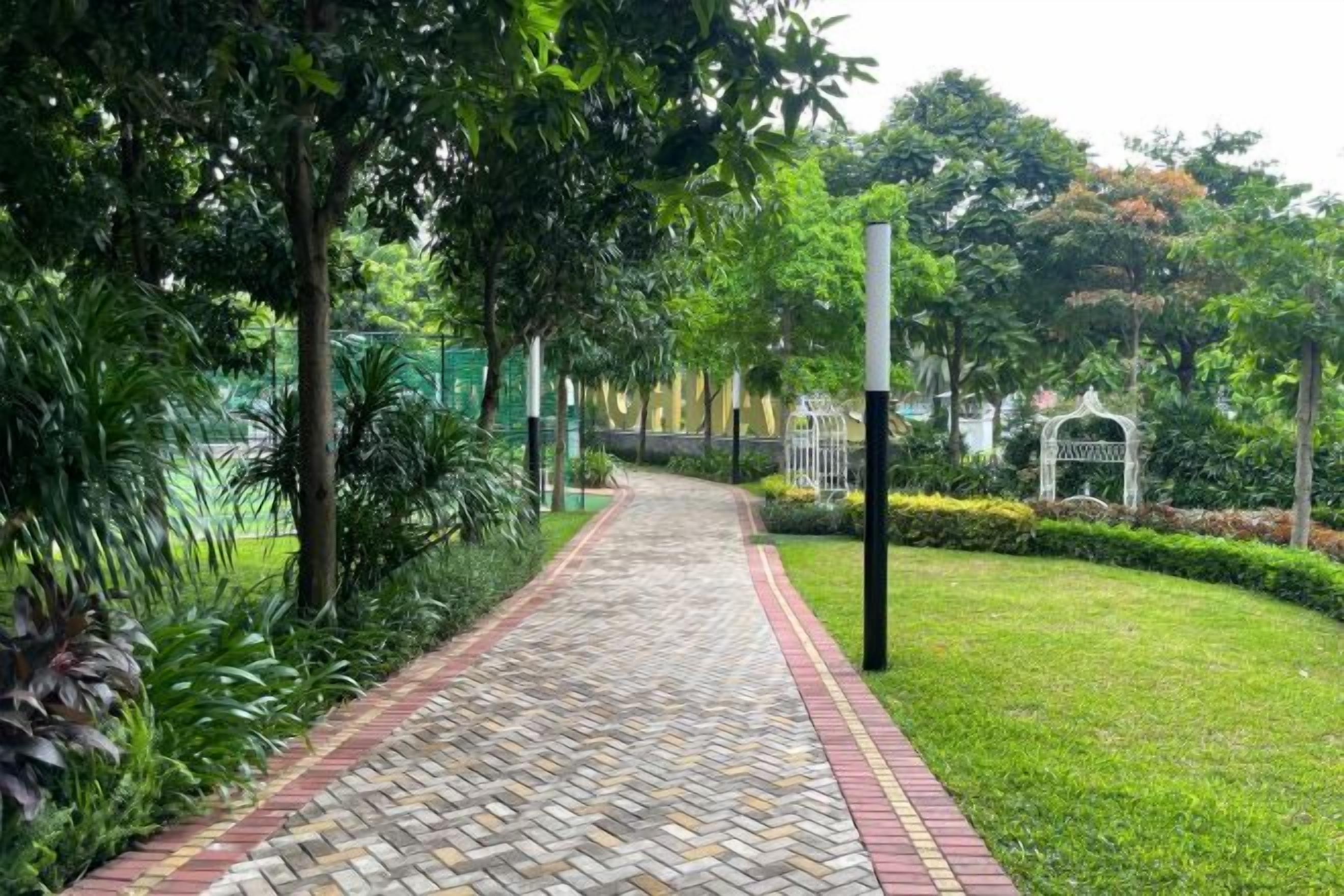 A paved pathway in a park-like setting with greenery on both sides.