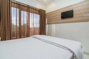 Habitación de hotel con cama, cortinas, televisor montado y vistas al exterior.