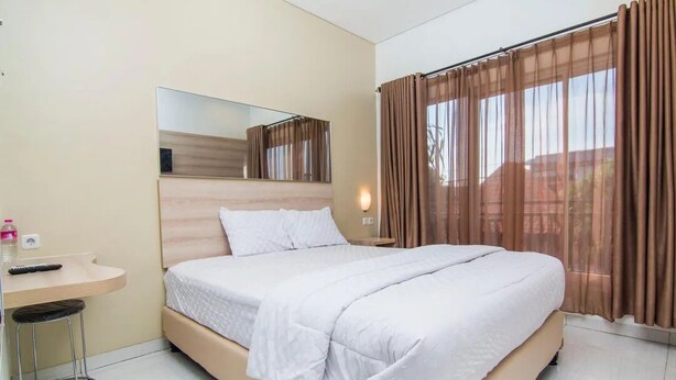 Une chambre à coucher avec un lit, une table de chevet, un miroir et une fenêtre avec des rideaux.