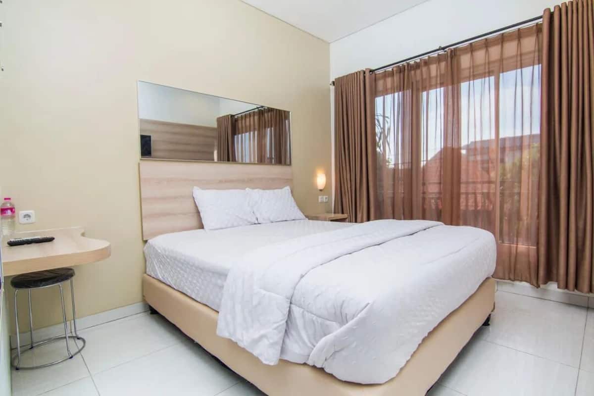 Een slaapkamer met een bed, nachtkastje, spiegel en raam met gordijnen.