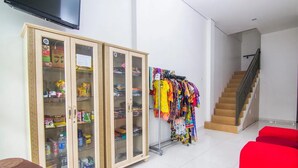 Une pièce comprenant un meuble renfermant des collations, un portant à vêtements avec des pièces colorées, un escalier et des sièges rouges.