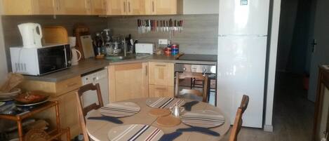A compact kitchen with wooden cabinets, a microwave, a refrigerator, and a dining table with placemats.