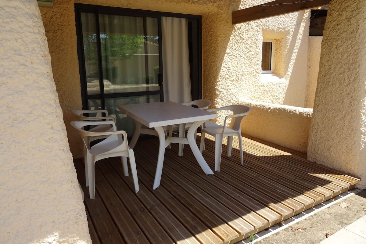 Eine Terrasse mit Tisch und Stühlen, ein Holzdeck und ein Gebäude mit strukturierter Wandfassade.