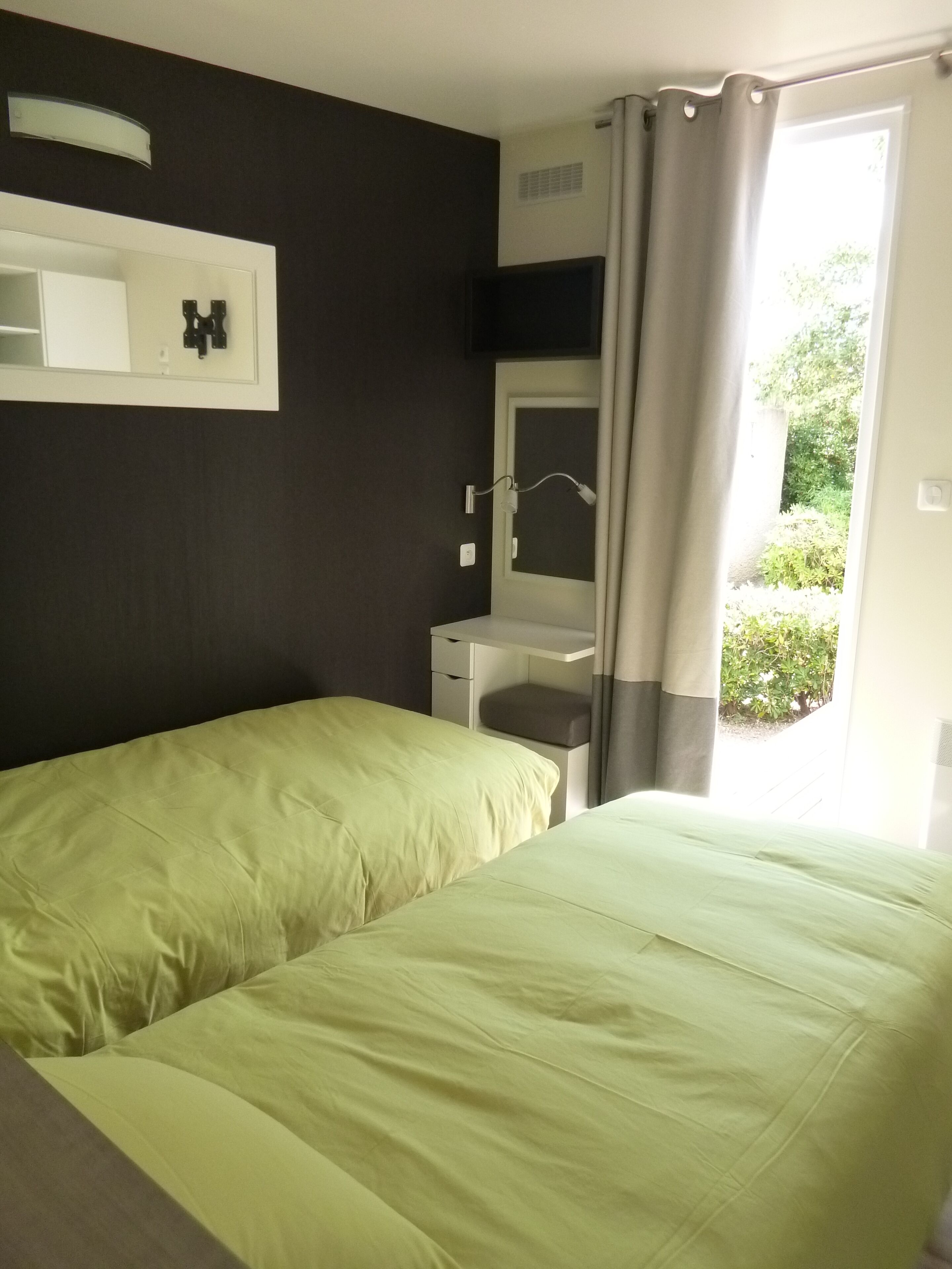A room with two beds, a desk, a mirror, and a window with curtains.