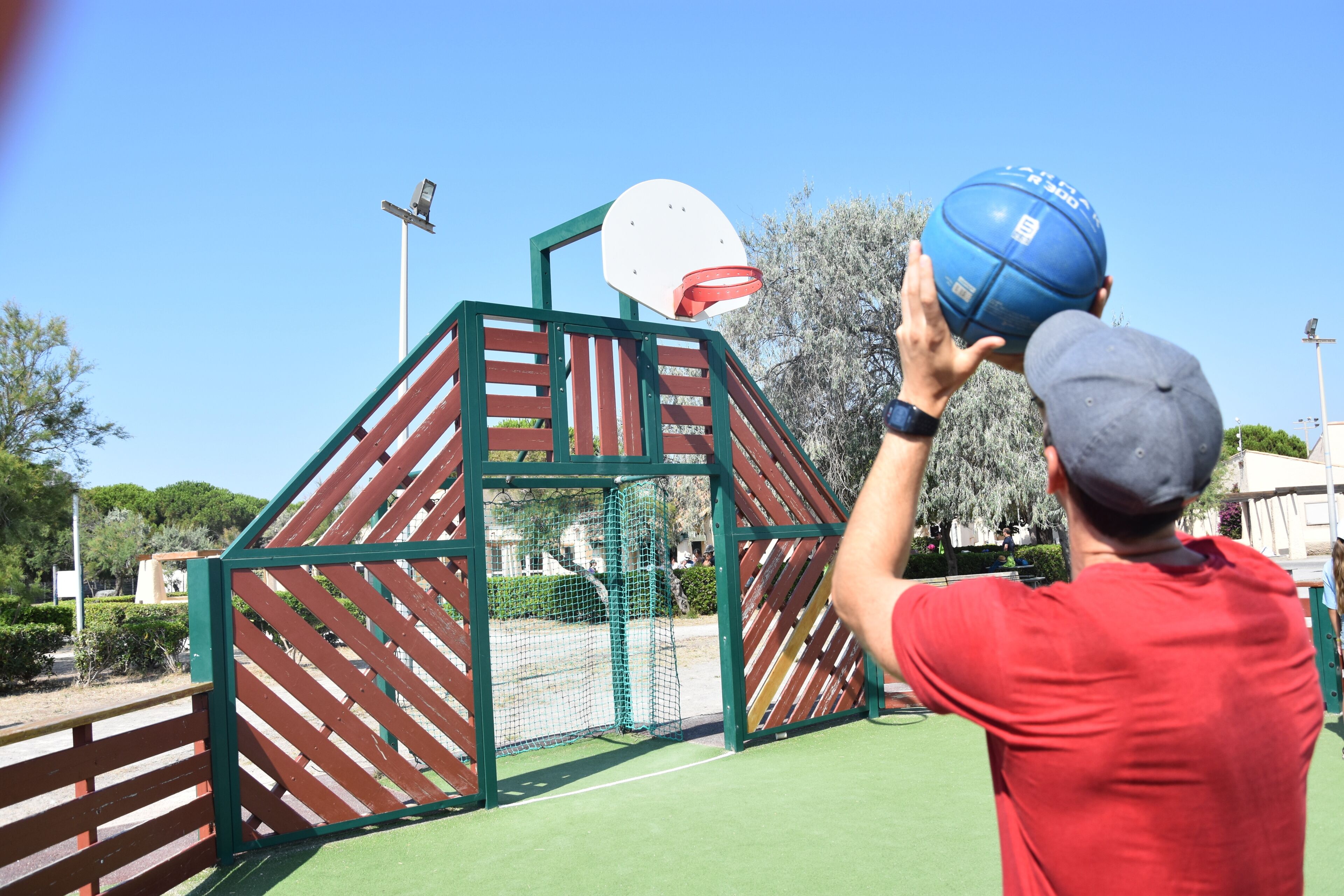 A basketball hoop with a net, a green and red play structure, and a clear blue sky.