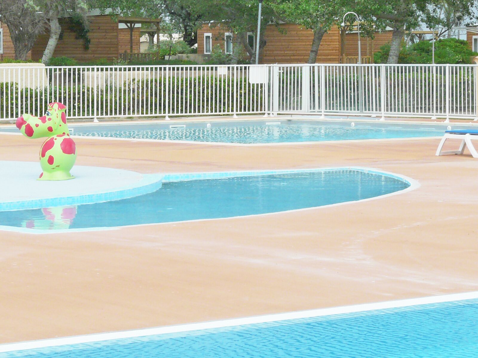 Ein Swimmingpool mit weißem Zaun und zwei tierförmigen Skulpturen in Grün und Rosa.