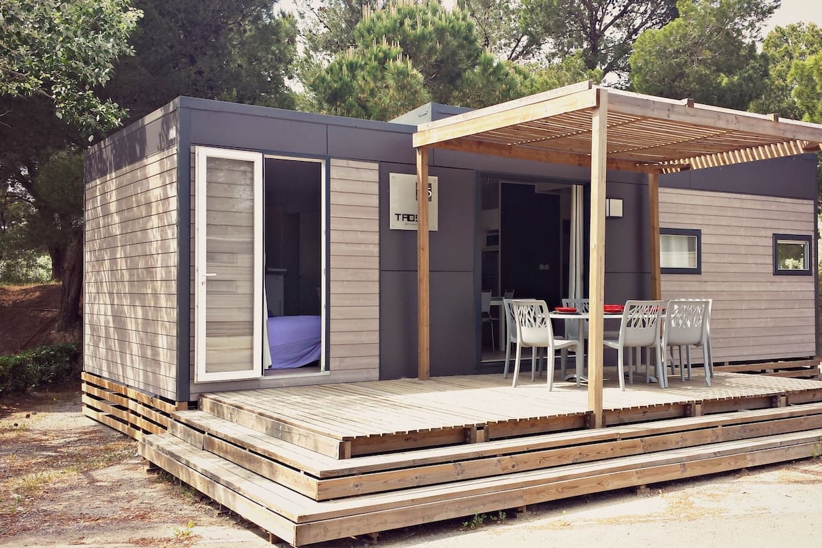 Eine moderne, kompakte Hütte mit offener Terrasse, Essbereich und Schlafbereich.