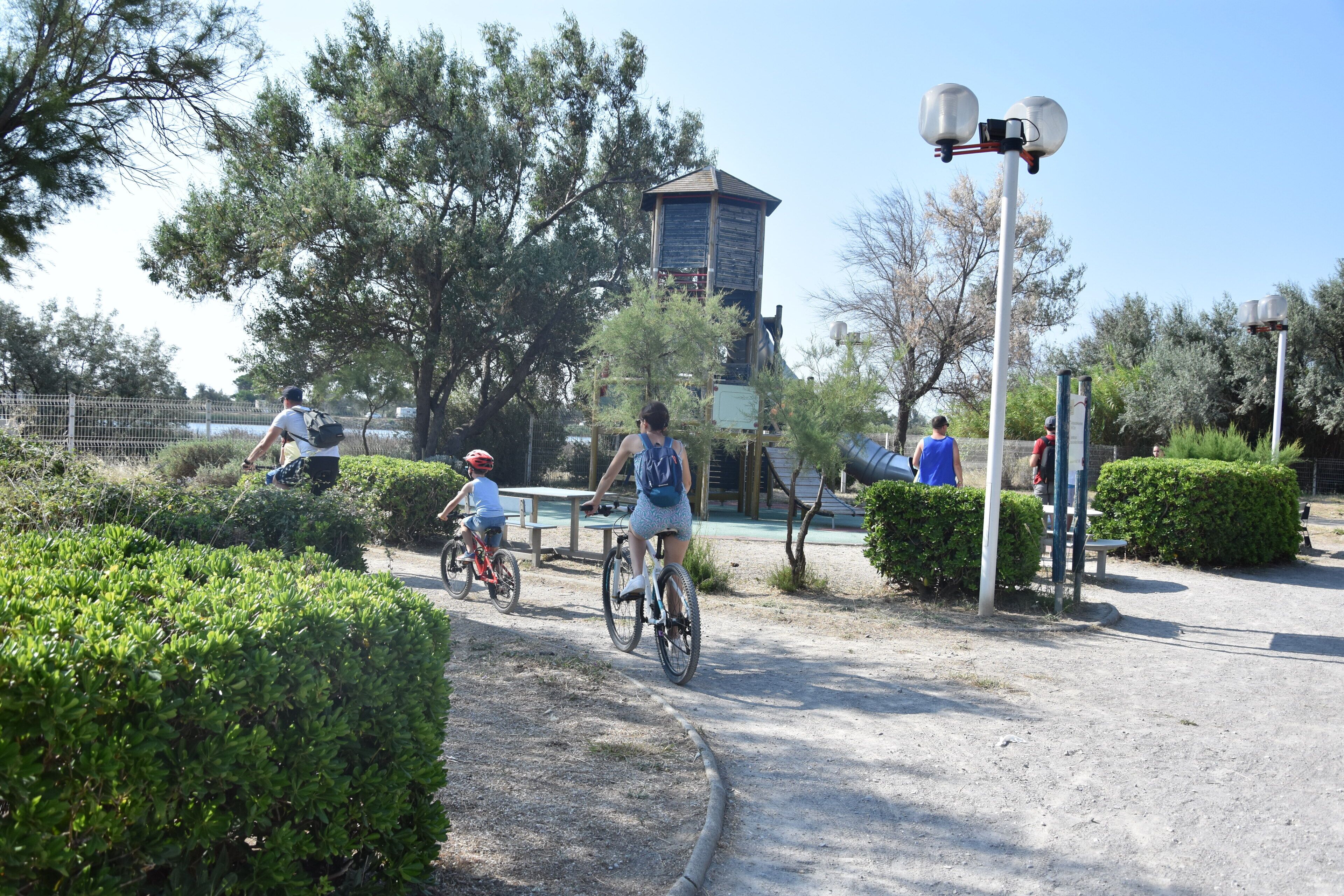 Um caminho pavimentado com ciclistas, rodeado por vegetação e um tanque de água ao fundo.