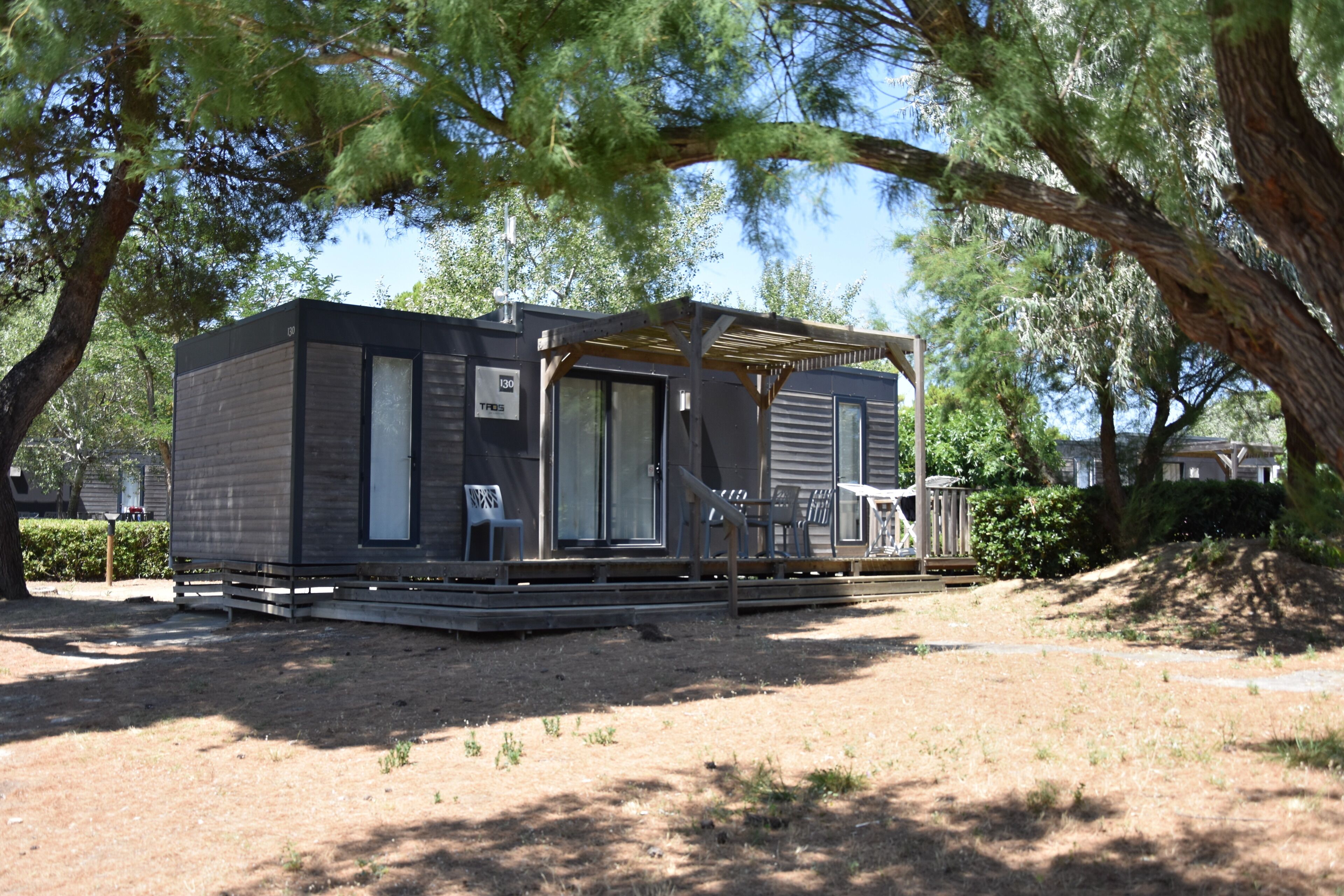 A small, single-story mobile home with a covered porch, a sliding door, and a patio area with chairs.