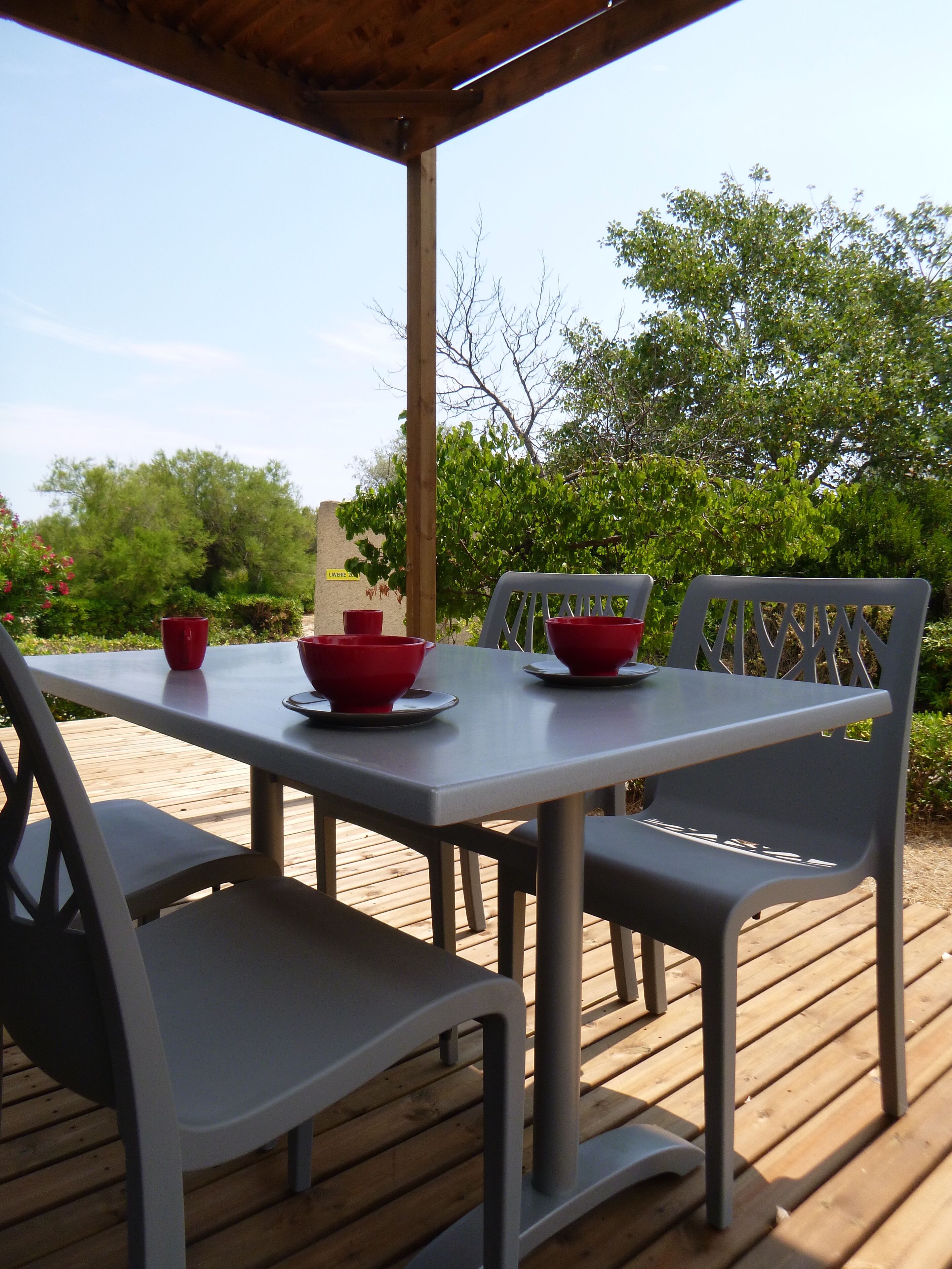 A covered outdoor dining area with a table and chairs, surrounded by greenery.