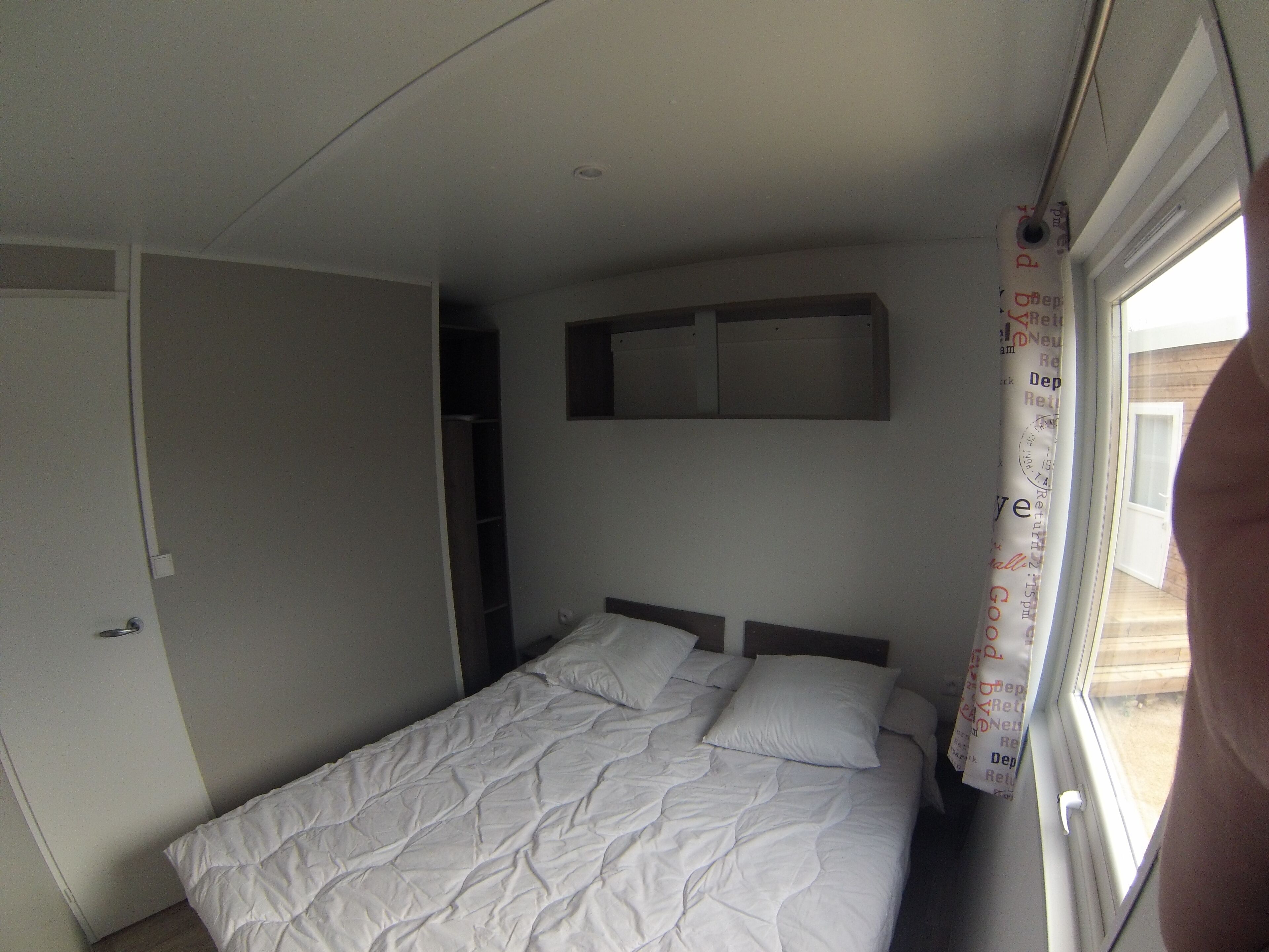 A bedroom with a bed, a wardrobe, and a window with a curtain.