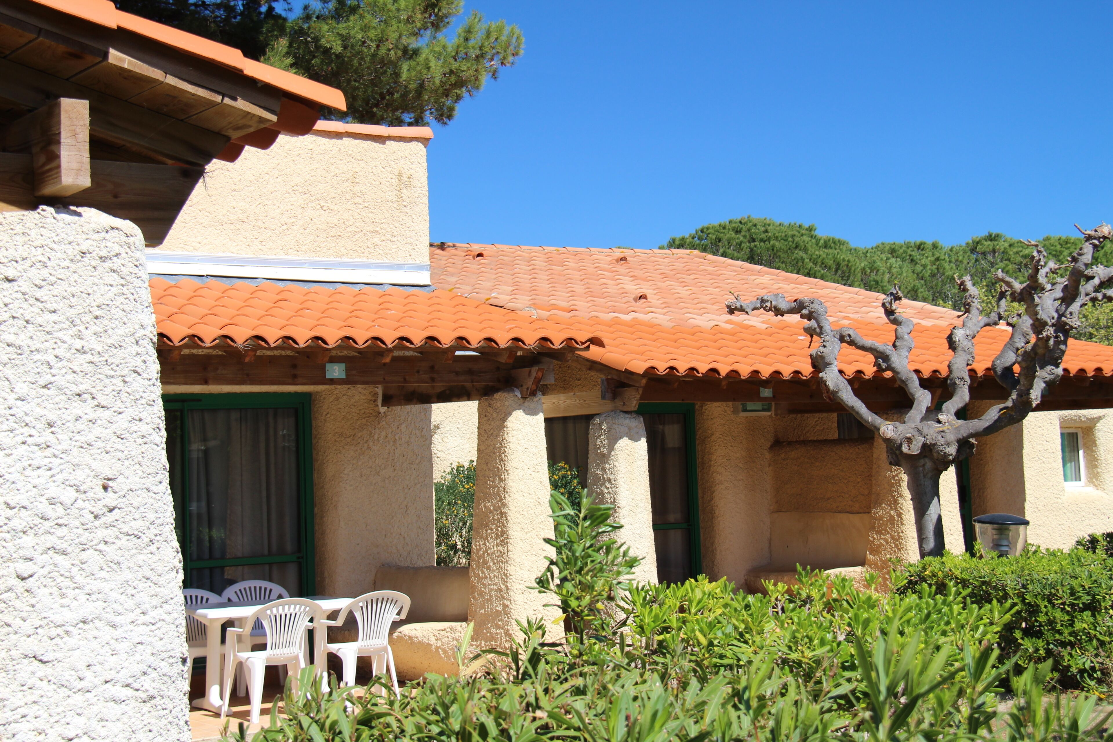 Un bâtiment avec un toit en tuiles, des places assises à l’extérieur et un arbre au premier plan.