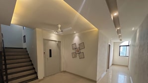 A spacious hallway with a staircase, a ceiling fan, recessed lighting, and framed artwork on the walls. - Shree Omkar Hotel (Indore)
