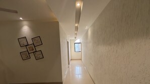 A hallway with a tiled floor, a ceiling fan, recessed lighting, and framed artwork on the wall. - Shree Omkar Hotel (Indore)
