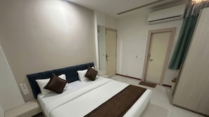 A hotel room with a bed, a bedside table, a wardrobe, an air conditioning unit, and a door. - Shree Omkar Hotel (Indore)