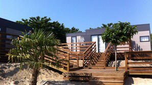 Ein Gebäude direkt am Strand mit hölzernen Treppen, die zu einem sandigen Bereich führen, umgeben von Palmen und moderner Architektur.