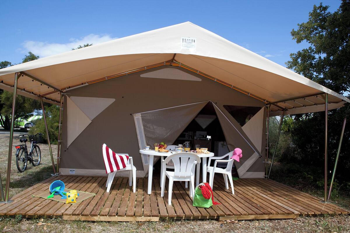 Une tente avec une table et des chaises, un vélo et une petite table sur laquelle sont disposés de la nourriture et des boissons.