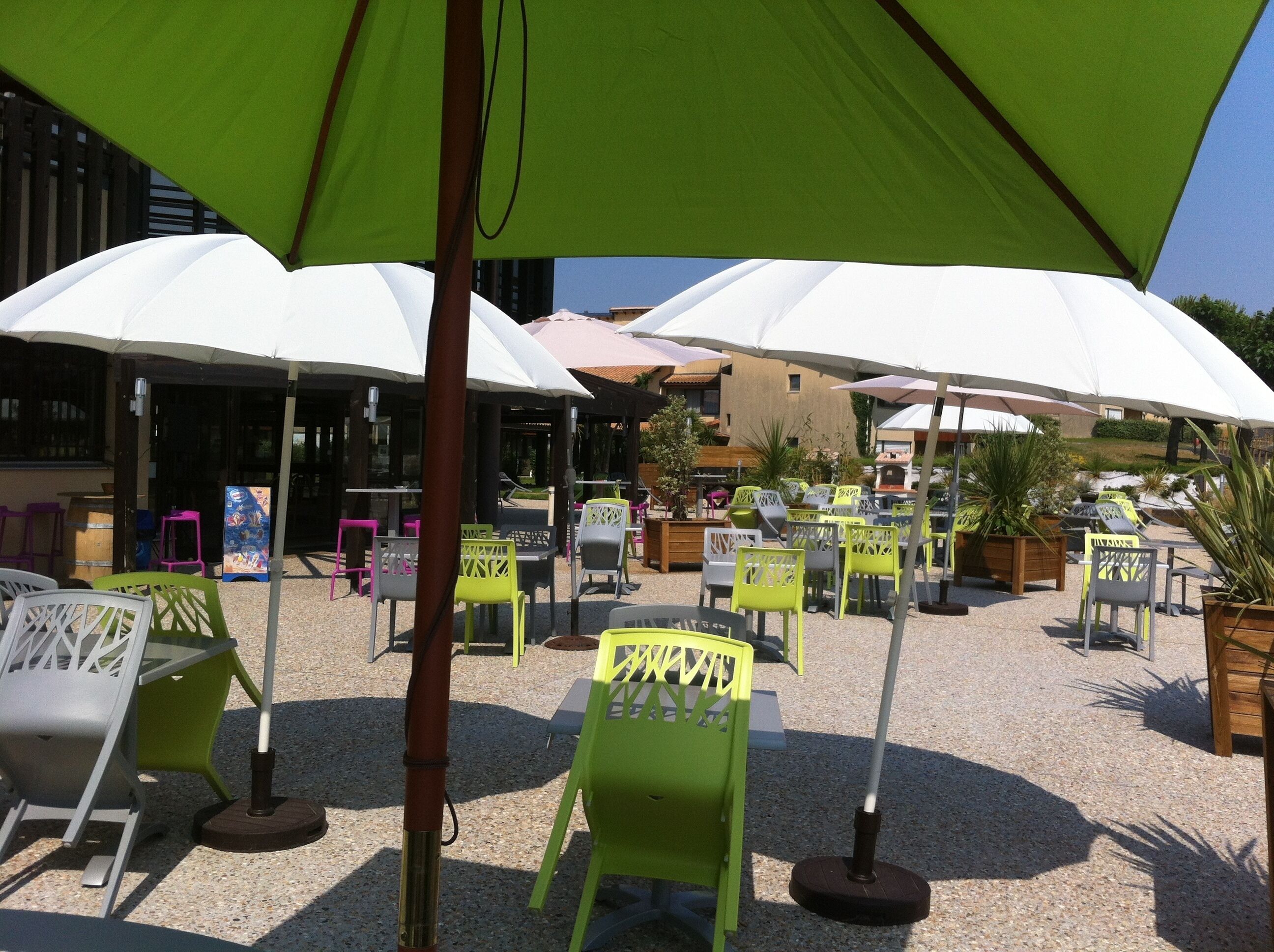 An outdoor seating area with tables and chairs under large umbrellas, surrounded by buildings.