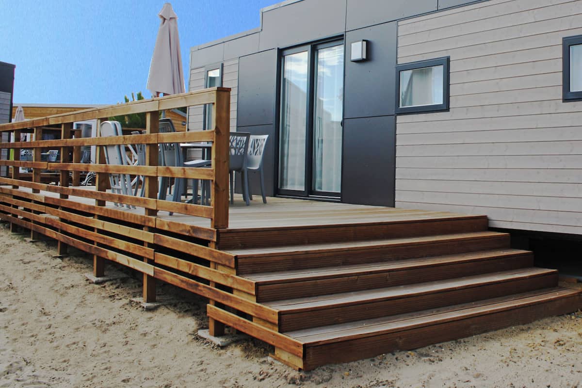 Un bâtiment moderne doté d’une terrasse en bois, de sièges extérieurs et d’une porte-fenêtre coulissante.
