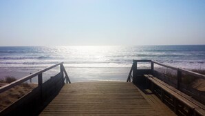 Ein Holzsteg führt zum Meer, wo Wellen auf die Küste branden.