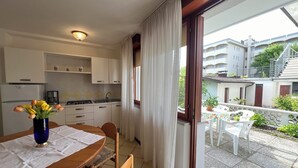 Eine Küche mit weißen Schränken, einem Esstisch mit Blumenvase und Blick auf einen Balkon mit Gartenmöbeln.