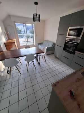 A kitchen with a dining table, chairs, a sofa, a microwave, and a stove. - T3 furnished near the beach (Pornichet)