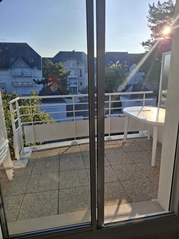 A balcony with a white railing, a small table, and a view of residential buildings. - T3 furnished near the beach (Pornichet)