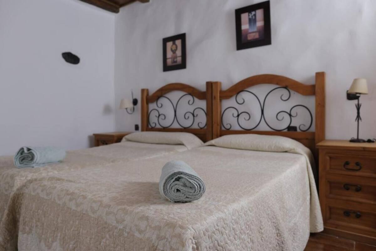 A neatly made bed with a rolled towel, a wooden headboard, a nightstand with a lamp, and two framed pictures on the wall.