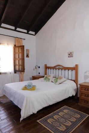 Une chambre à coucher avec un lit en bois, une table de chevet, une commode, une fenêtre avec des rideaux et un tapis à motifs.