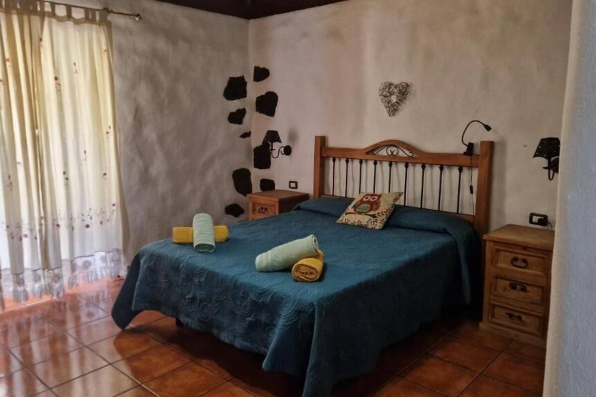 A bedroom with a bed, bedside tables, a nightstand, a wall decoration, and a curtain.