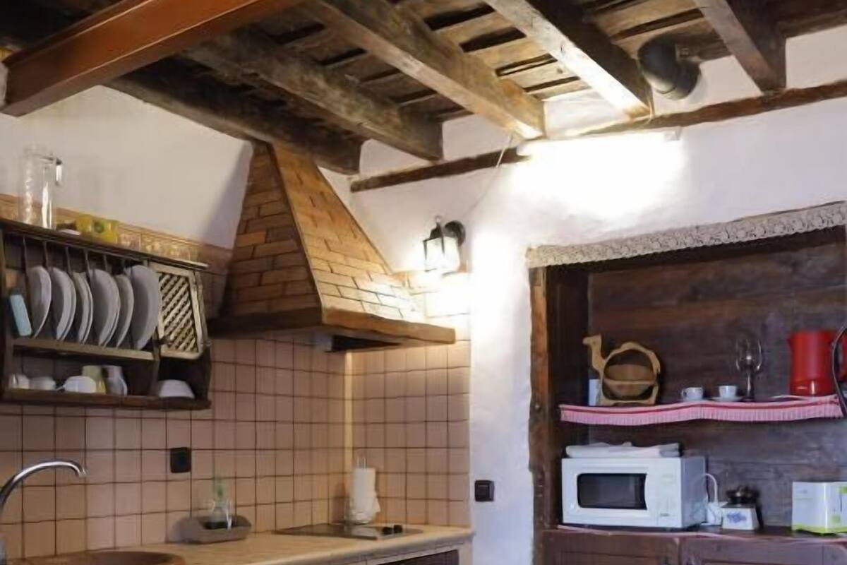 A kitchen with a tiled backsplash, wooden cabinets, a built-in microwave, and a small trash bin.