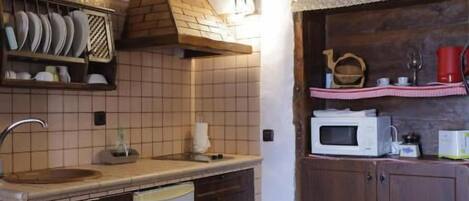 Una cocina con salpicadero de azulejos, armarios de madera, microondas integrado y un pequeño cubo de basura.