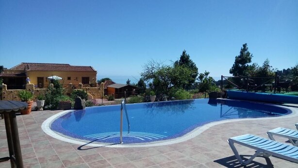 A swimming pool with a tiled deck, lounge chairs, and a building in the background. - Finca Casonas de Marengo (Icod de los Vinos)